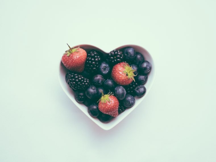 bowl of blueberries and strawberries in a love heart shaped bowl on a blue plain background
