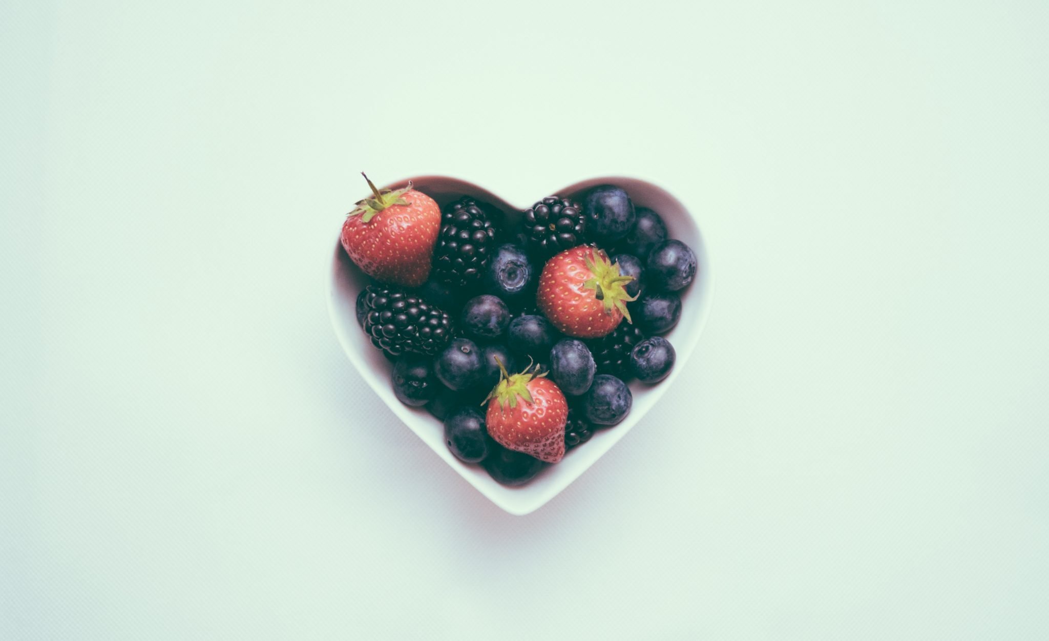 bowl of blueberries and strawberries in a love heart shaped bowl on a blue plain background