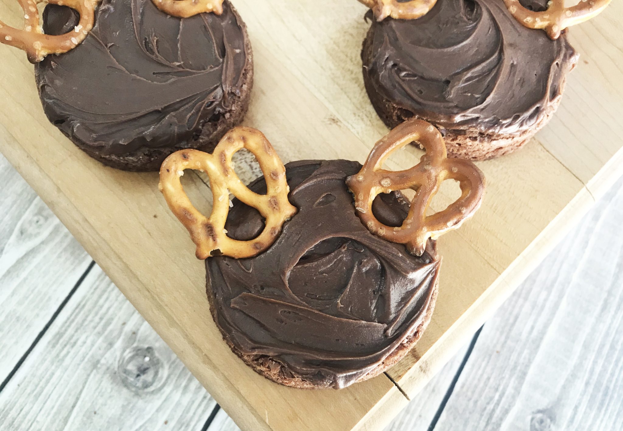 circular reindeer brownie cutouts with frosting and pretzel antlers on chopping board with white background