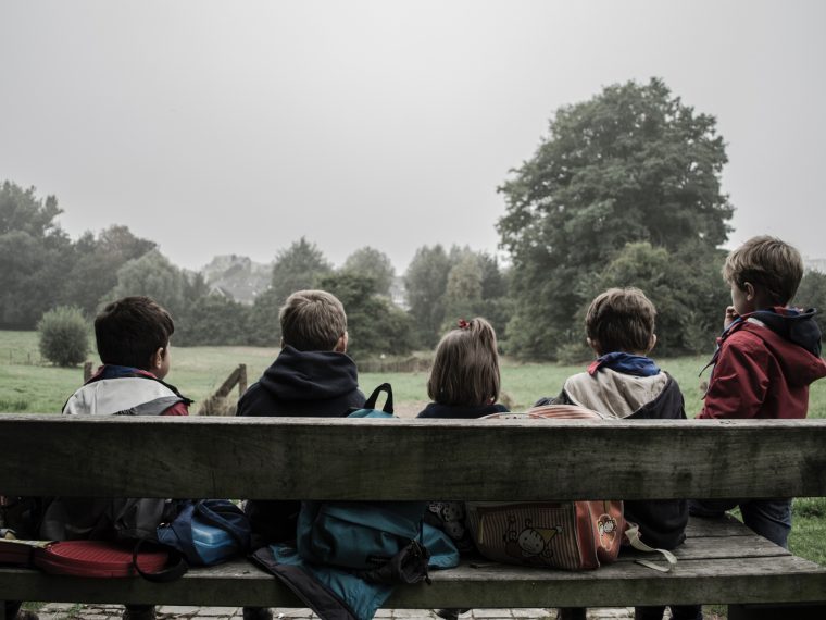 groups of kids facing away from the camera sitting on a bench at the park on a grey day.